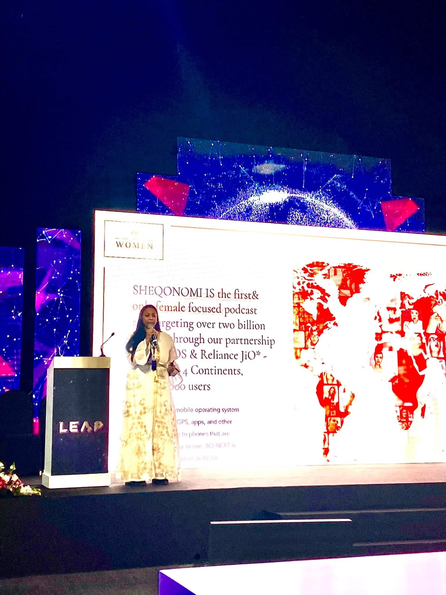 Anu Bhardwaj on stage presenting SHEQONOMI's global reach — "SHEQONOMI IS the first & only female-focused podcast targeting over two billion through our partnership with JIO & Reliance JiO — 4 Continents" · LEAP Summit, Riyadh, February 2022