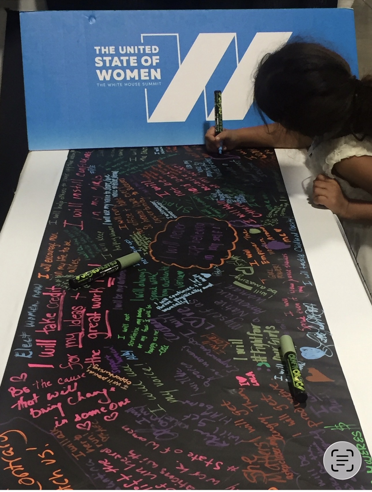 Arya Bhardwaj writing on the chalkboard pledge wall at The United State of Women Summit, 2016