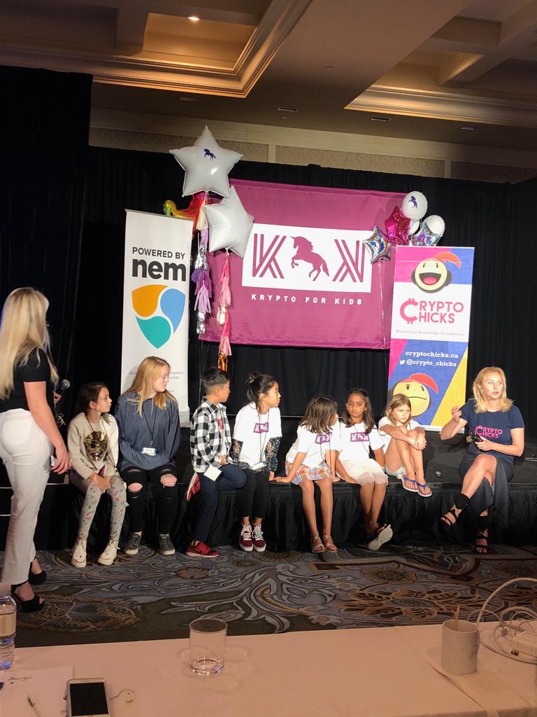 Krypto for Kids kids panel on stage — children seated in front of the Krypto for Kids banner, NEM (Powered by NEM) and CryptoChicks banners, Blockchain on the Beach, Montage Resort Laguna Beach, November 2018.